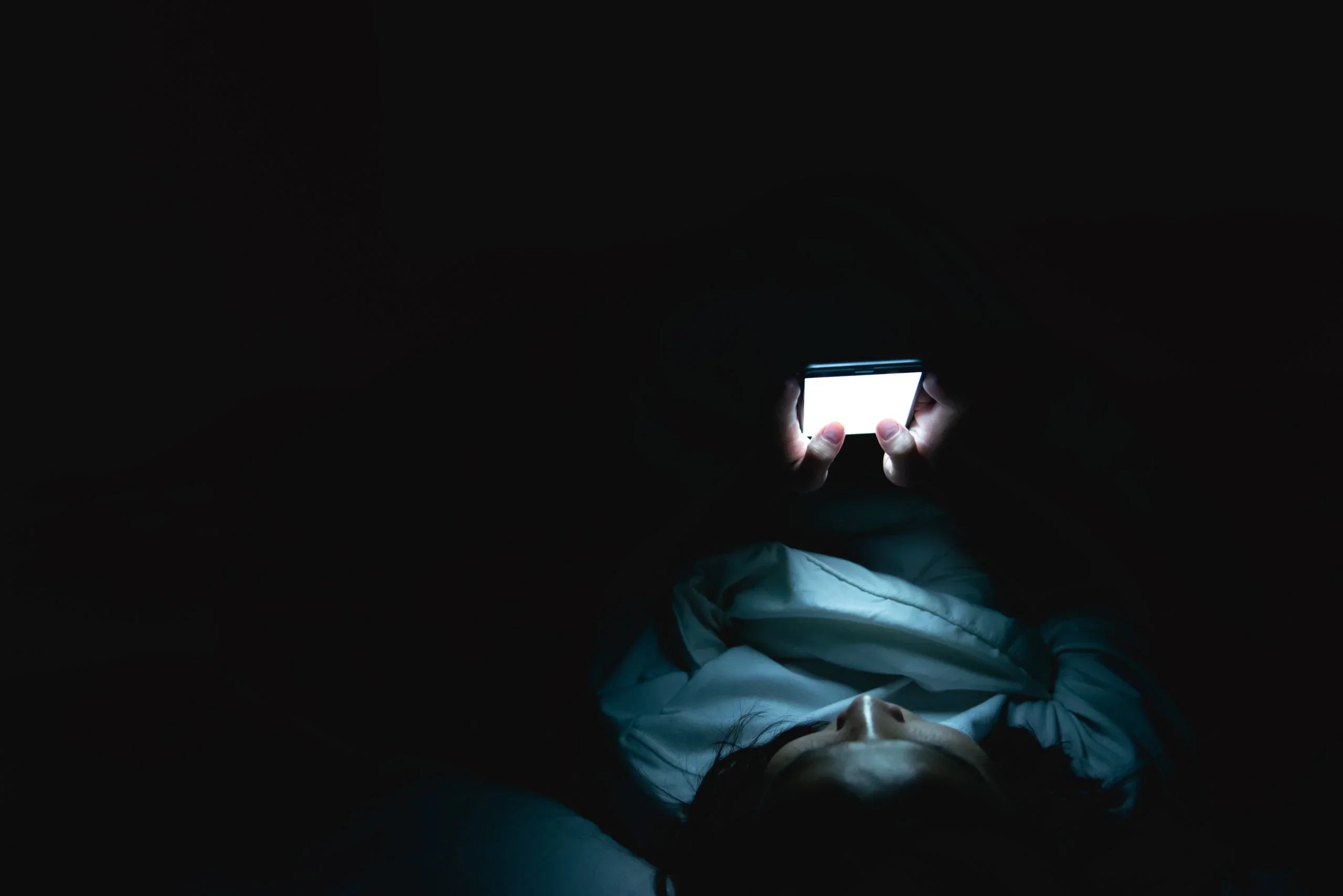 Person lying in bed at night using smartphone with bright screen in dark room
