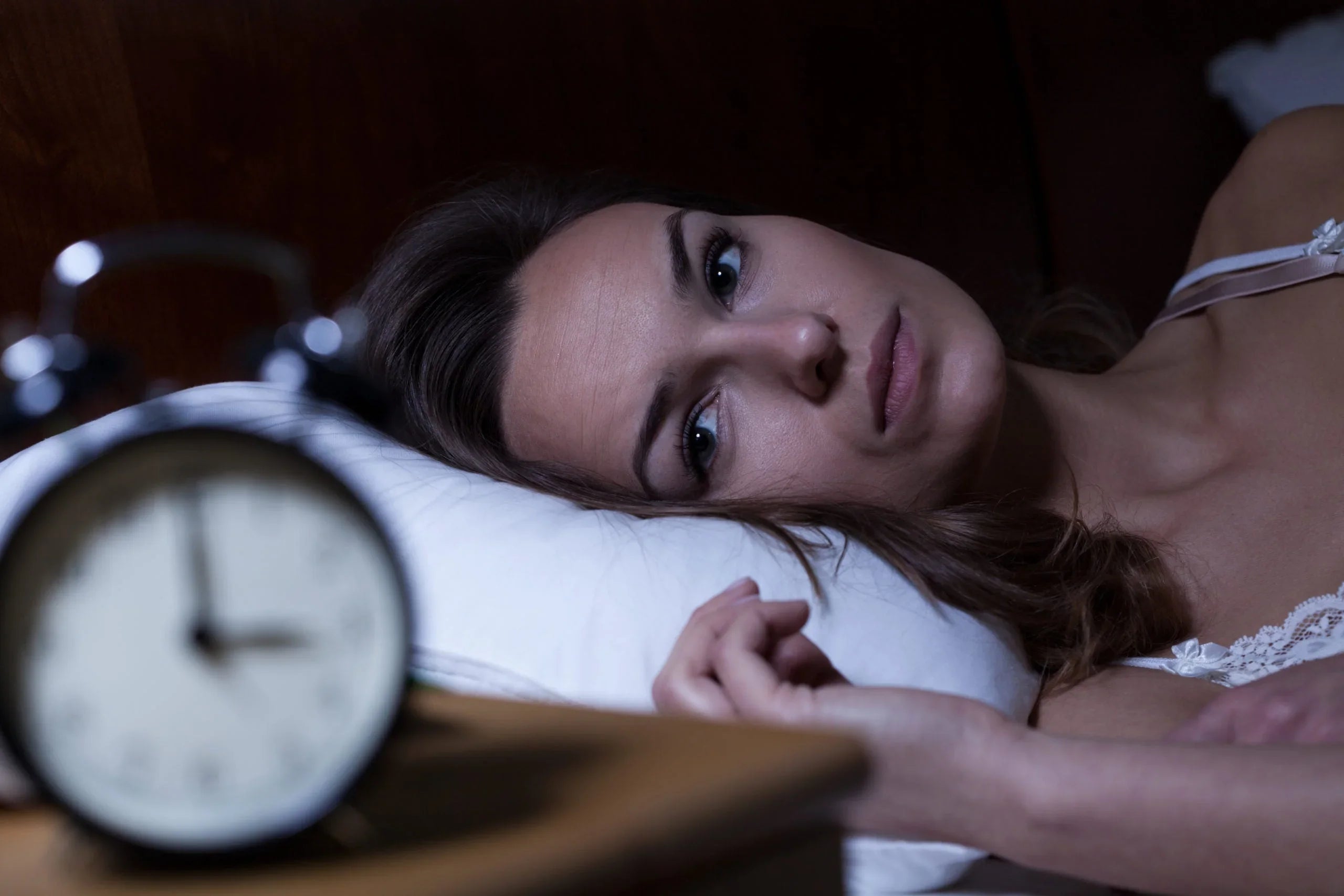 Woman lying awake in bed at night with vintage alarm clock showing 3:30 AM
