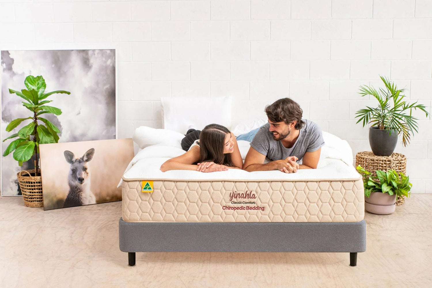 Couple lying on Yinahla Classic Comfort orthopedic mattress in modern bedroom with plants and kangaroo artwork