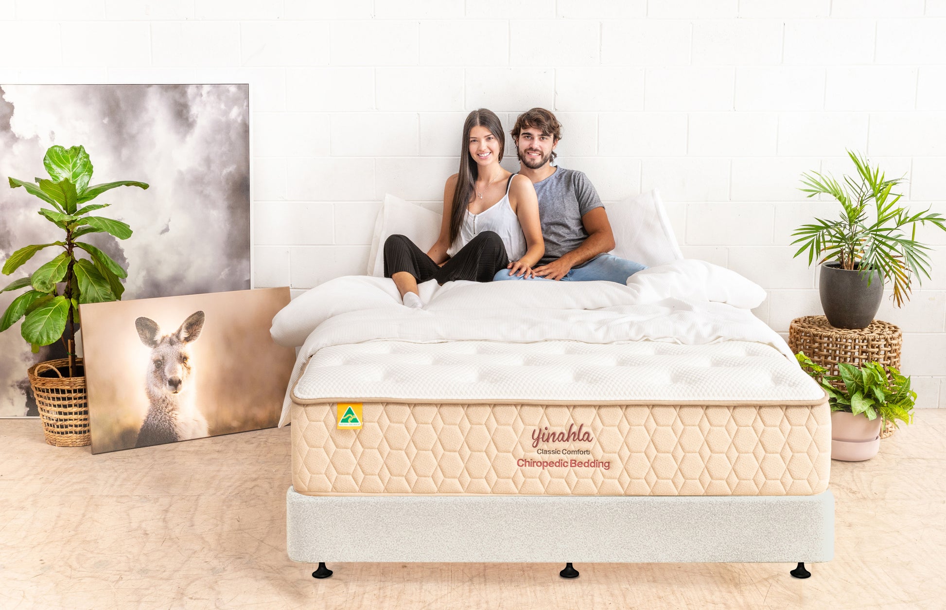 Young couple sitting on yinahla Classic Comfort Chiropedic mattress in bright, stylish bedroom with plants and kangaroo photo