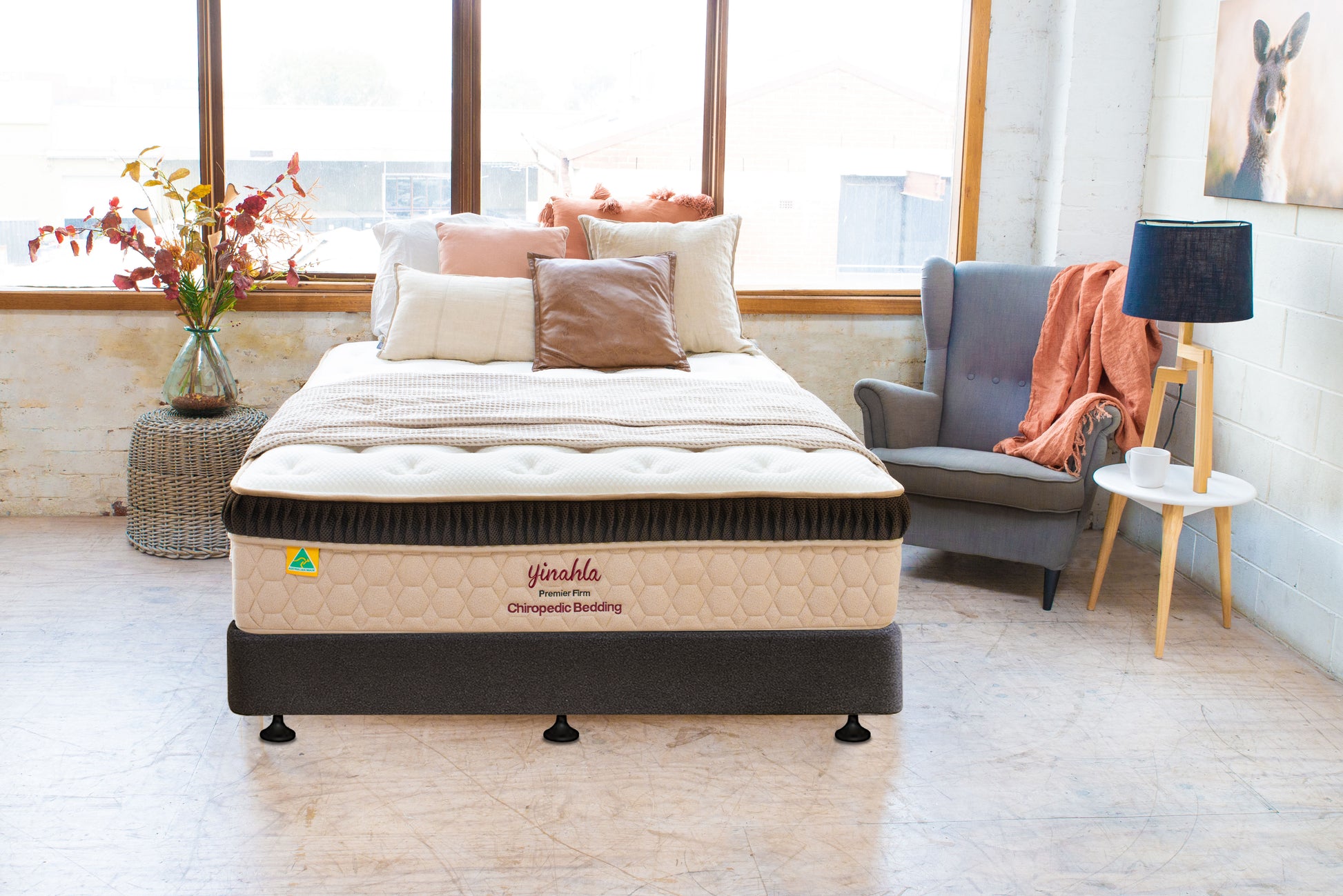 Premier firm chiropractic mattress with beige and brown bedding in a bright bedroom with gray armchair and side table