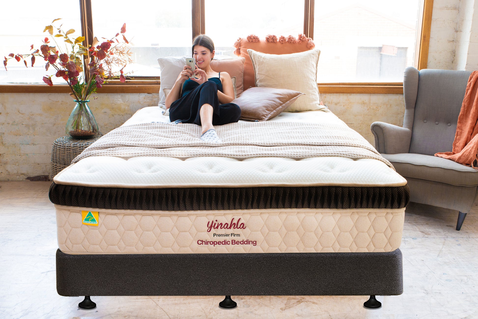 Woman relaxing on Yinahla Premier Firm Chiropedic Bedding mattress in bright, cozy bedroom with decorative pillows