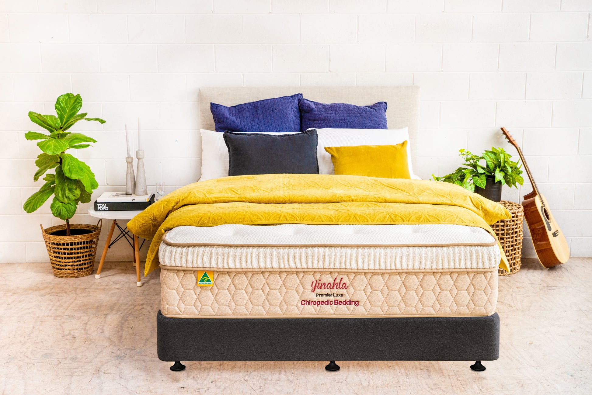Yinahla Premier Luxe orthopedic mattress with yellow and blue bedding, indoor plants, and acoustic guitar