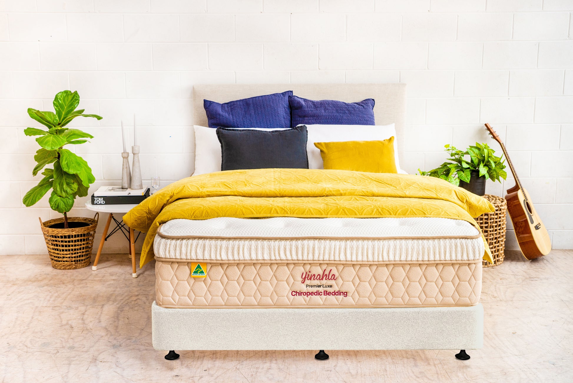 Modern bedroom with Premier Luxe chiropractic bed, yellow and blue pillows, green plants, and guitar