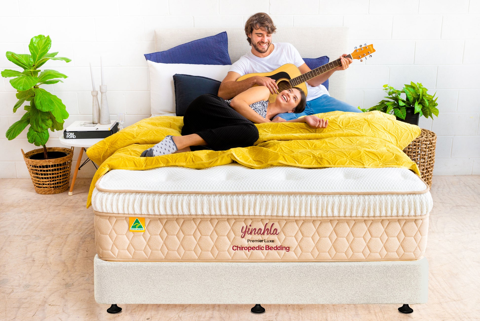 Couple relaxing on a Yinahla Premier Luxe orthopedic mattress with yellow bedding in a bright bedroom