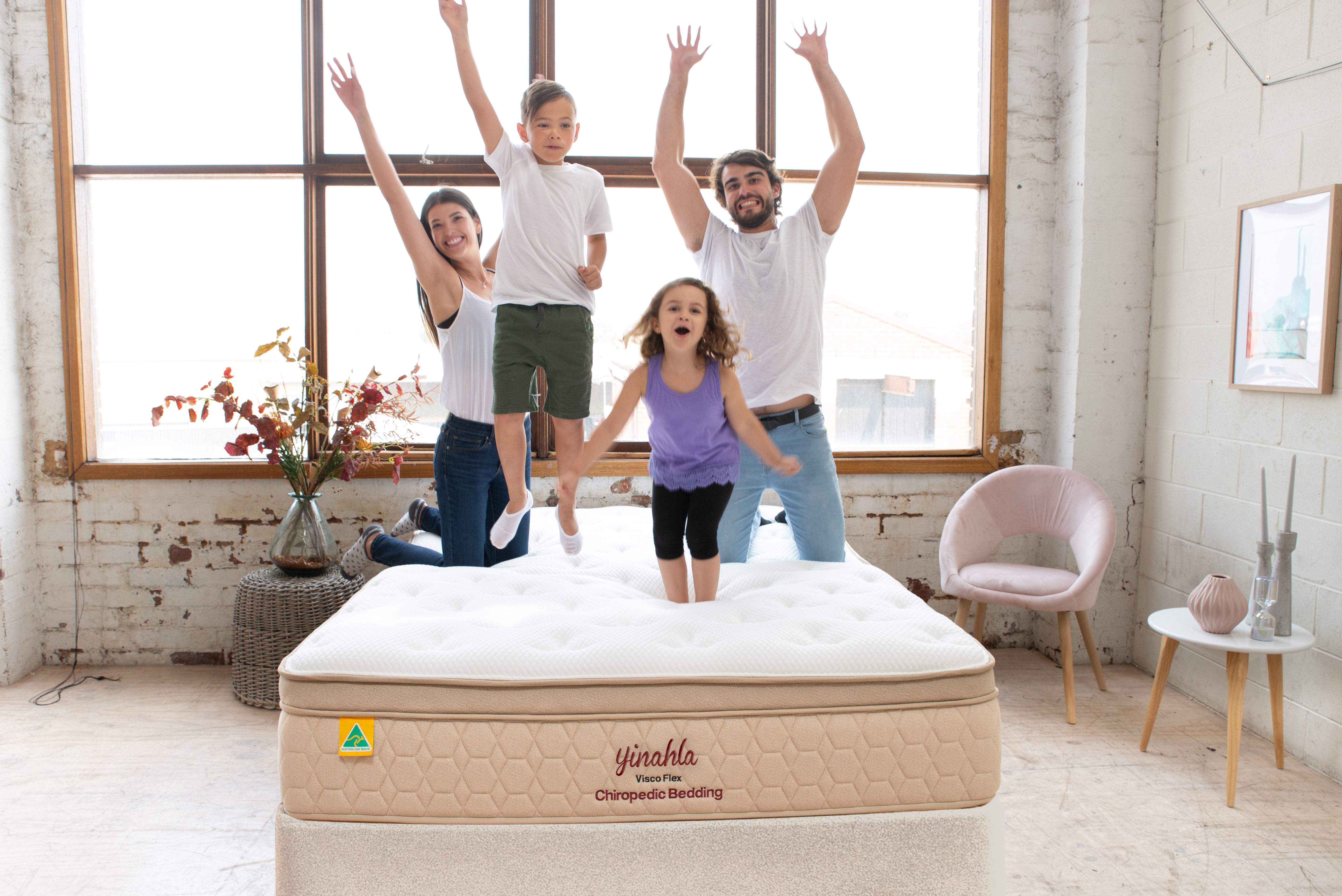 Happy family jumping on a Yinahla Visco Flex Chiropedic Bedding mattress in a bright, modern bedroom