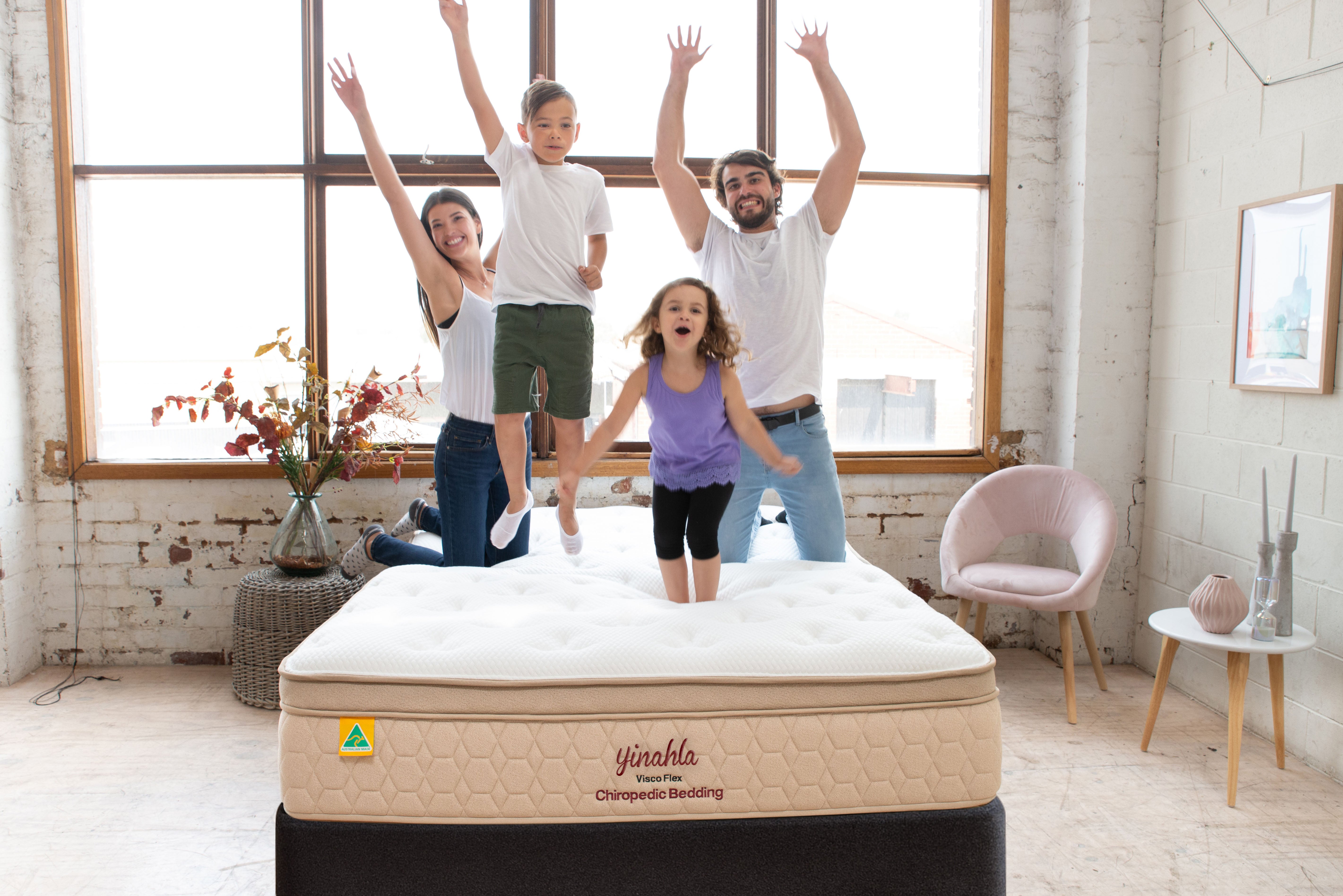 Happy family jumping on a Yinahla Visco Flex orthopedic mattress in bright loft bedroom