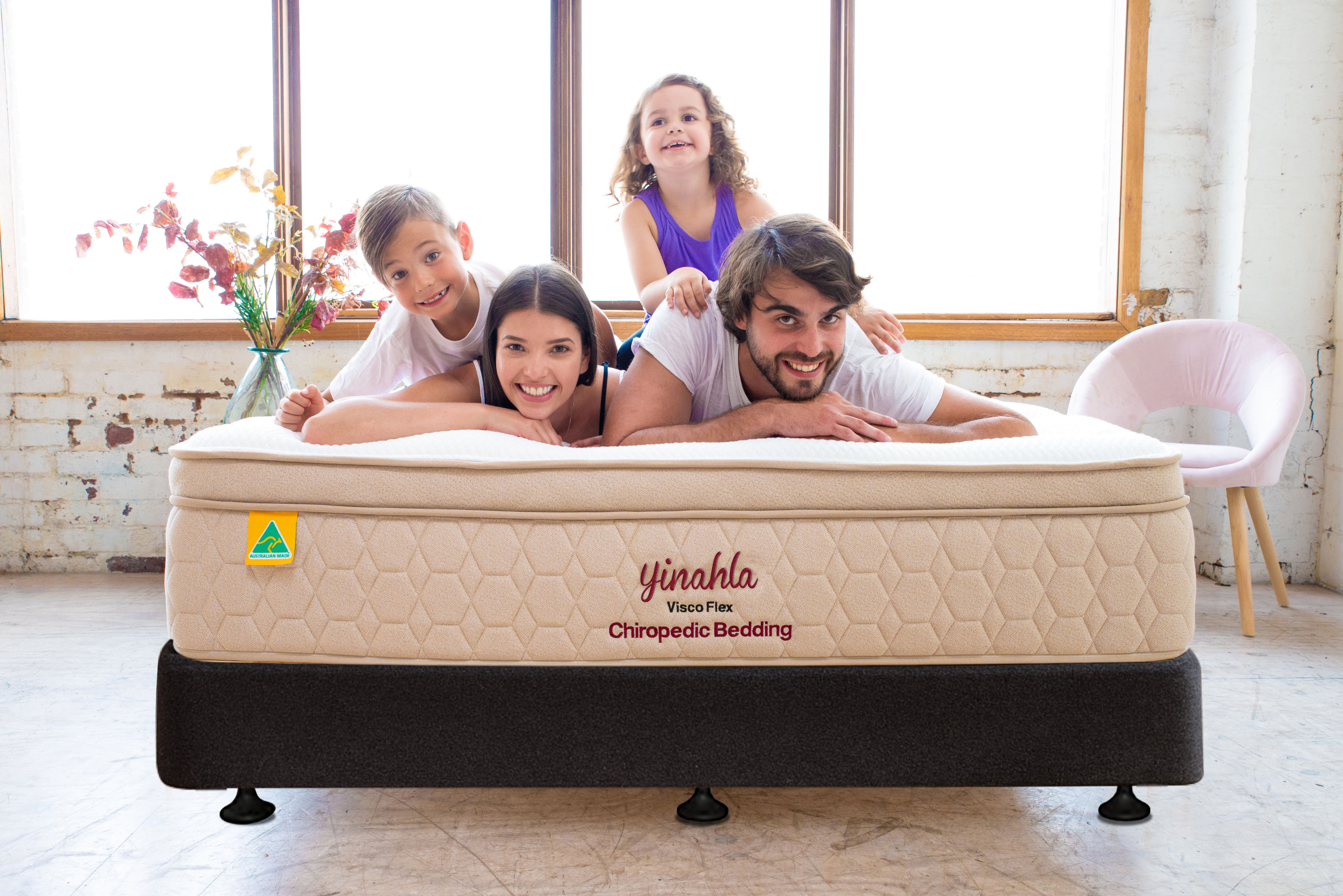Happy family of four on Yinahla Visco Flex Chiropedic mattress in bright room with large windows